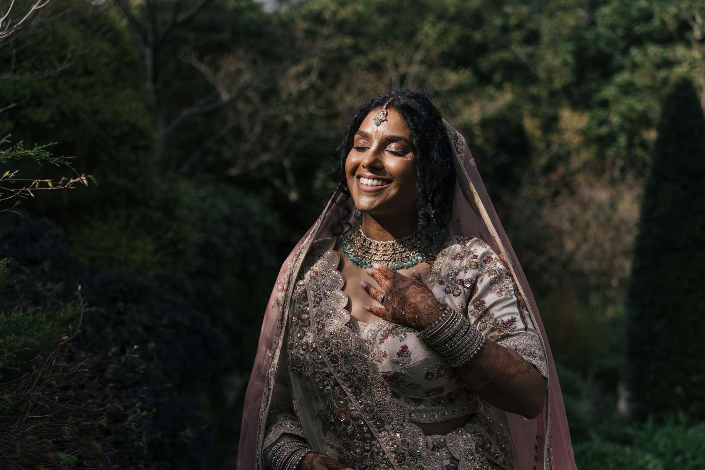 A bride smiling with her eyes closed in warm sunlight